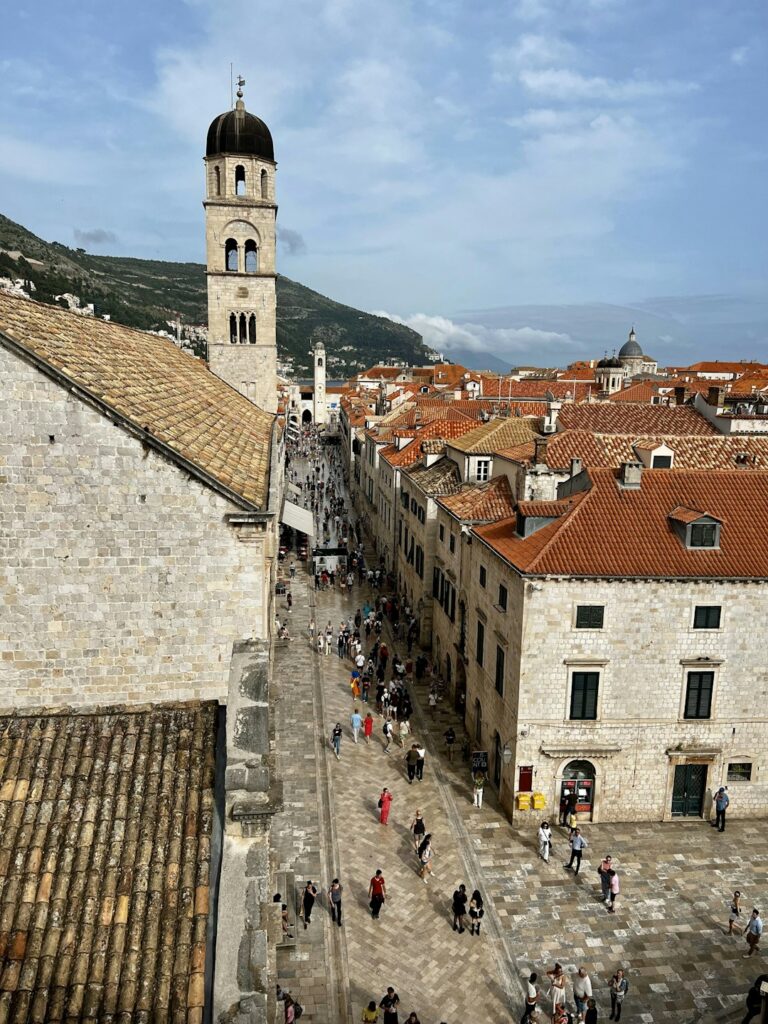 Unusual Places to Stay in Dubrovnik โ Travel Guide to Dubrovnik 140 a group of people walking down a street next to tall buildings