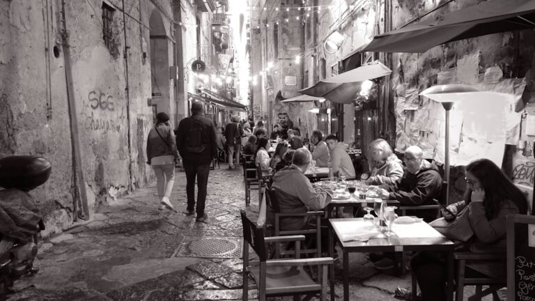 a group of people sitting at tables in a narrow alleyway