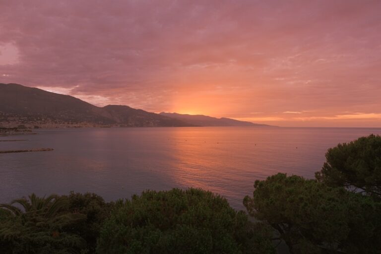 A sunset over a body of water with a mountain in the background